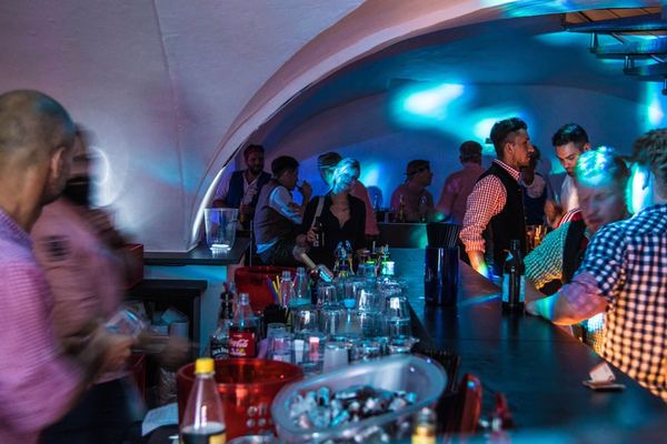 Gäste an der Bar unter blau beleuchtetem Gewölbe