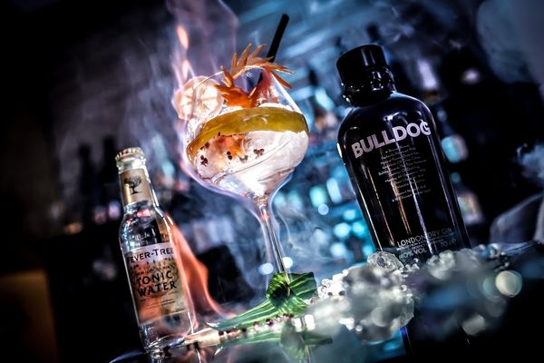 Gin-Cocktail mit Blüte neben Gin-Flasche und Tonic