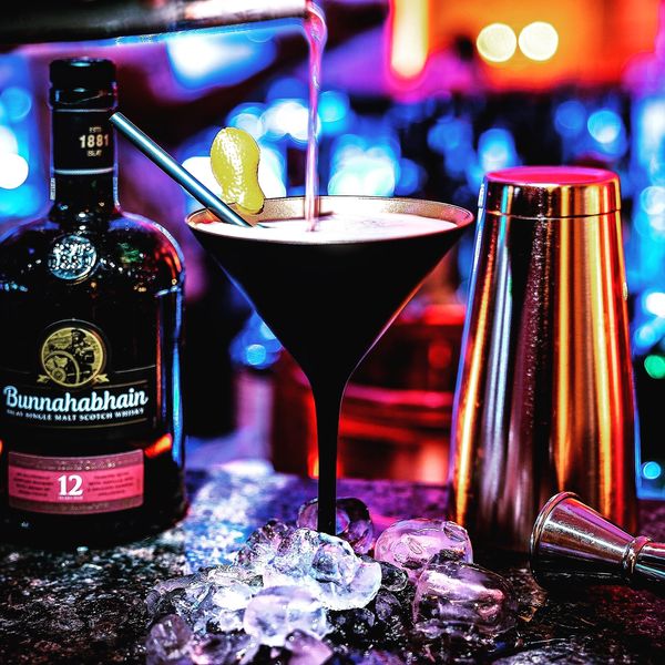Dunkler Martini-Cocktail neben Whisky-Flasche und Shaker